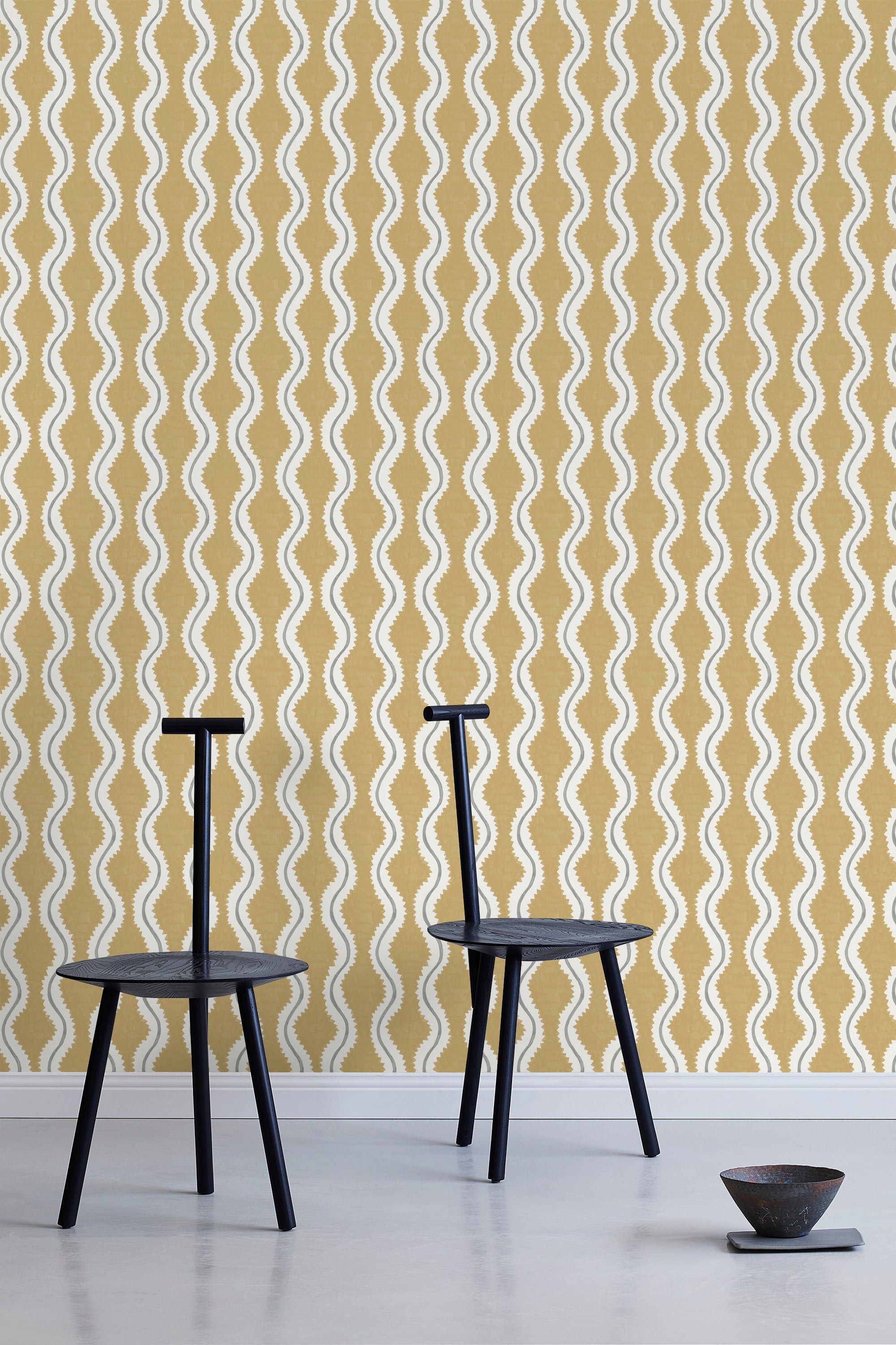 Two minimalist black chairs stand in front of a wall papered in a playful curvy stripe print in white, gray and mustard.