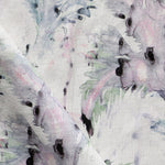 Detail of fabric in a painterly palm leaf print in shades of green, purple and gray on a cream field.