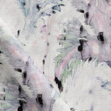 Detail of fabric in a painterly palm leaf print in shades of green, purple and gray on a cream field.