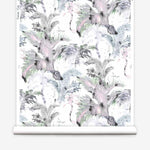 Partially unrolled wallpaper yardage in a painterly palm tree print in shades of gray, pink and green on a white field.