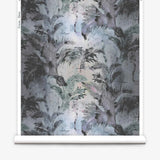 Partially unrolled wallpaper yardage in a painterly palm tree print in shades of gray and blue on a white field.