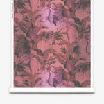 Partially unrolled wallpaper yardage in a painterly palm tree print in shades of red, pink and gray.