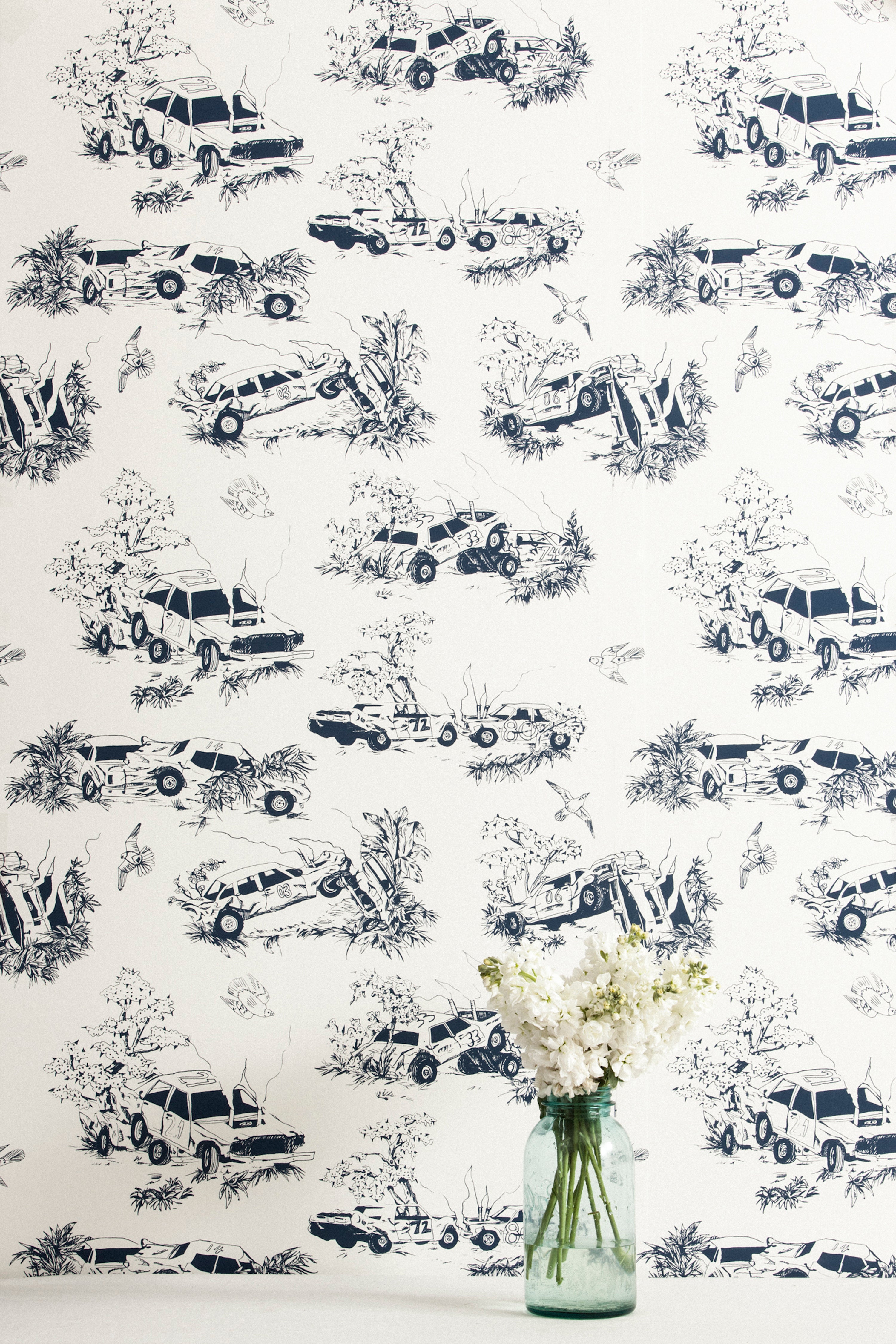 A vase of flowers stands in front of a wall covered in a playful illustrated car crash print in navy on a white field.