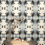 A modernist end table with flowers stands in front of a wall papered in a watercolor ink blot print in charcoal, gray and tan.