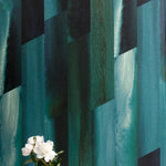 A vase of flowers stands in front of a wall papered in a linear geometric print in shades of black, blue and turquoise.