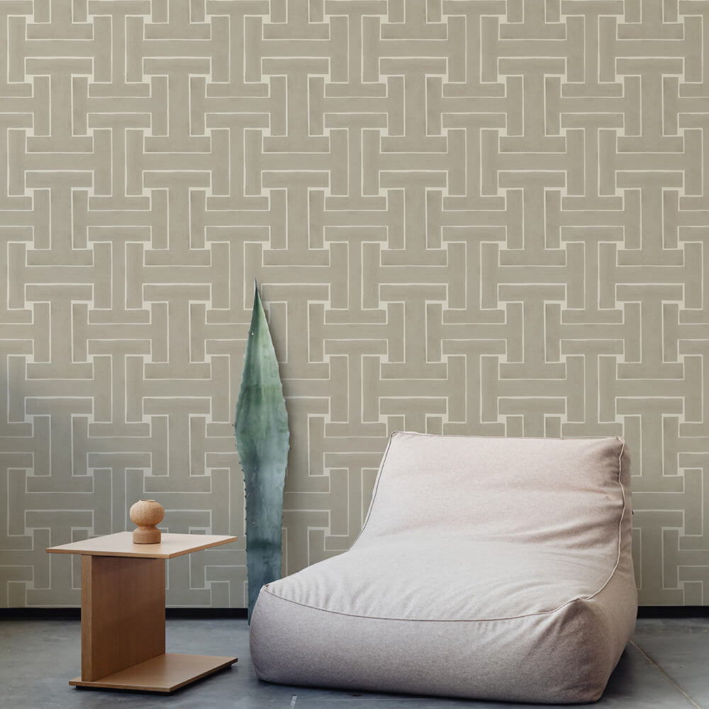 A plush chair and end table stand in front of a wall papered in a large-scale geometric print in tan and cream.