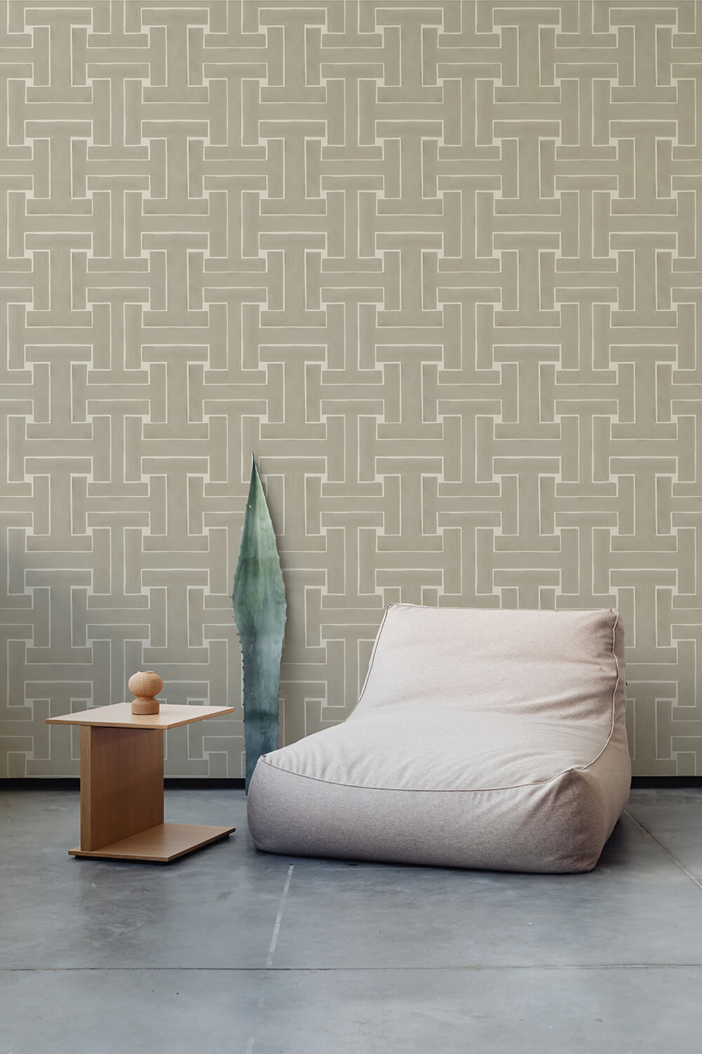 A plush chair and end table stand in front of a wall papered in a large-scale geometric print in tan and cream.