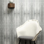 A modernist chair stands in front of a wall papered in a watercolor textural print in shades of gray.