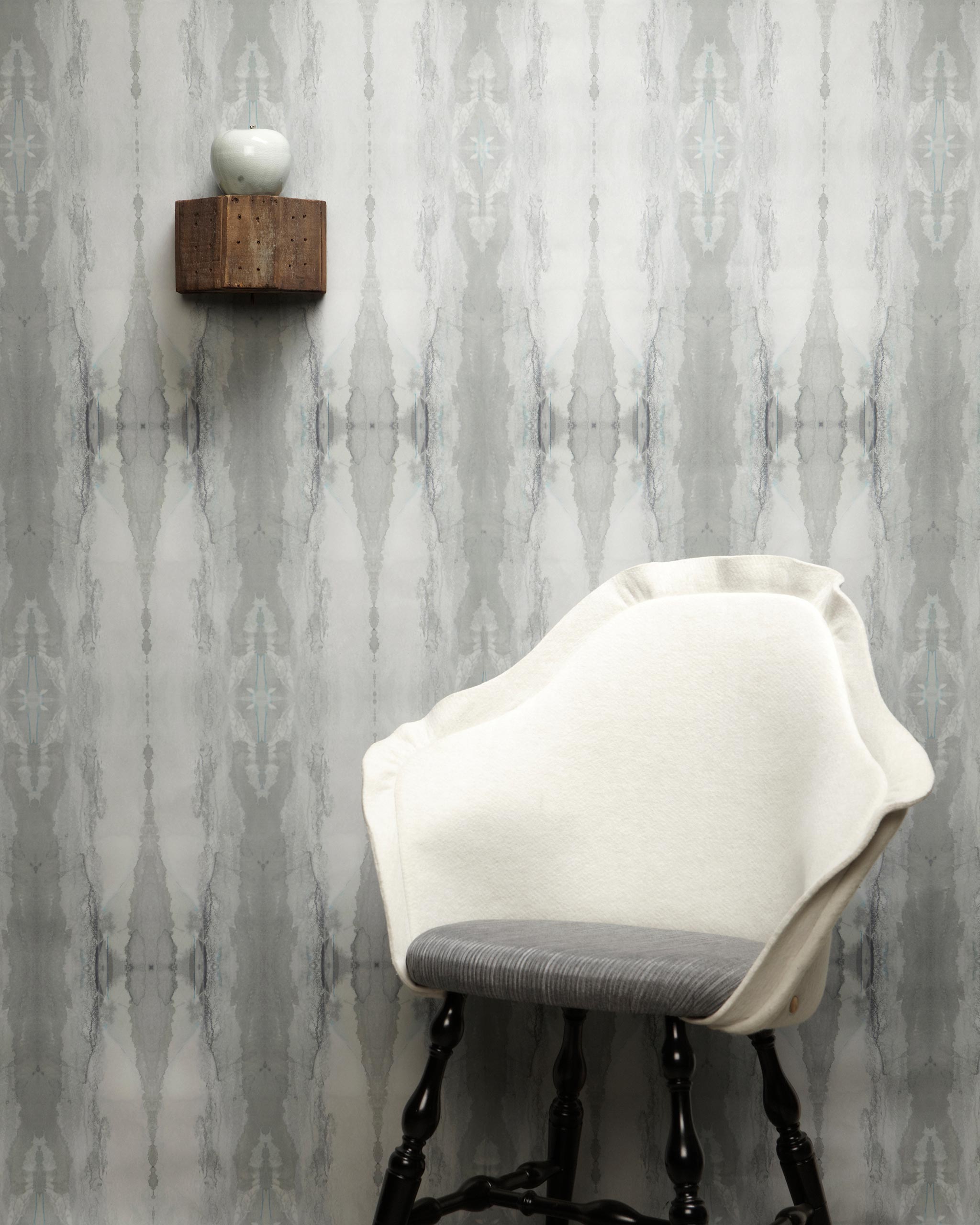 A modernist chair stands in front of a wall papered in a watercolor textural print in shades of gray.
