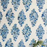 A vase of flowers stands in front of a wall papered in a painterly floral print in shades of blue and navy on a cream field.