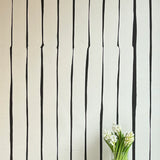 A vase of flowers stands in front of a wall covered in a playful irregular stripe print in black on a cream field.