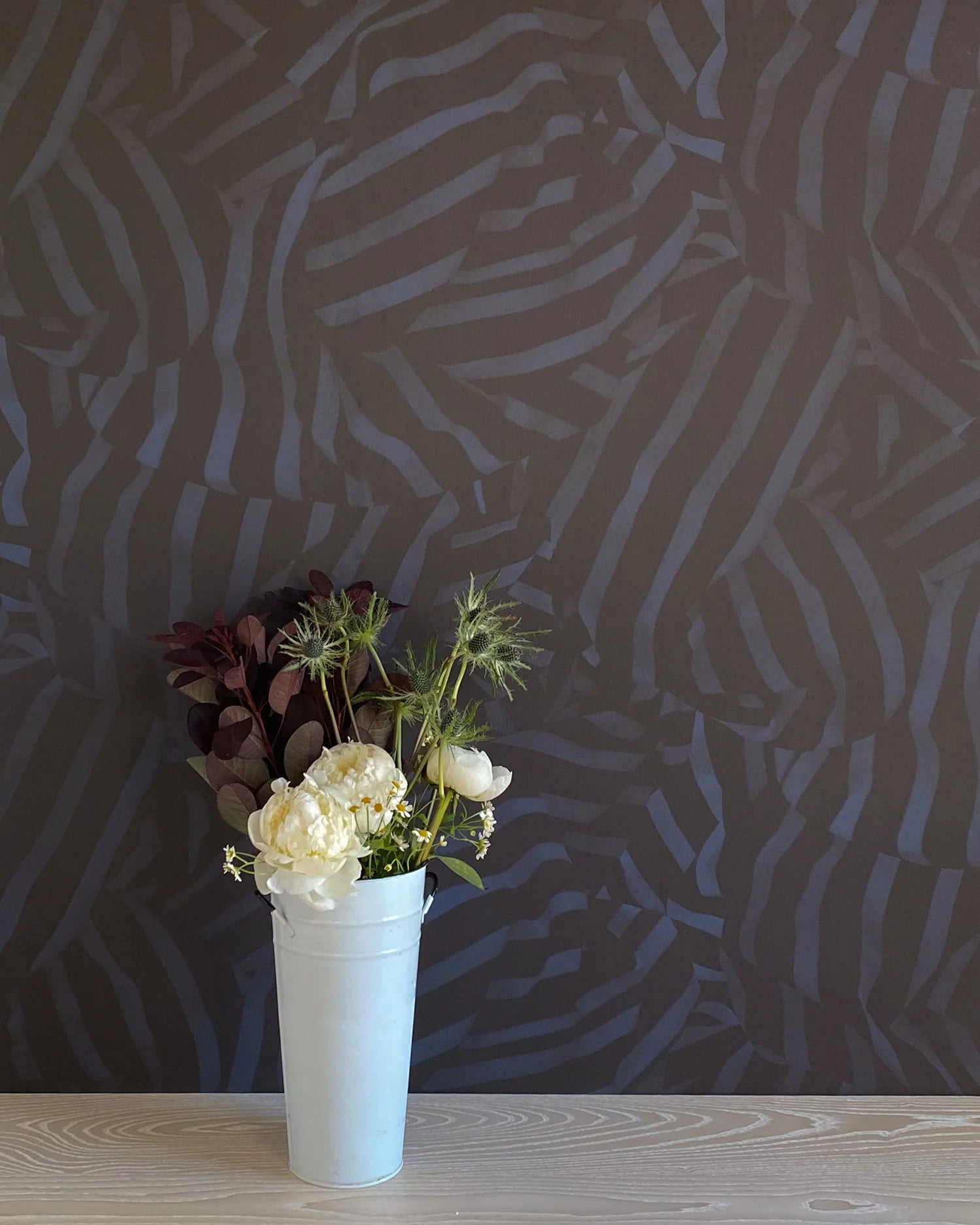 A vase of flowers stands in front of a wall papered in a playful broken stripe print in black on a navy field.
