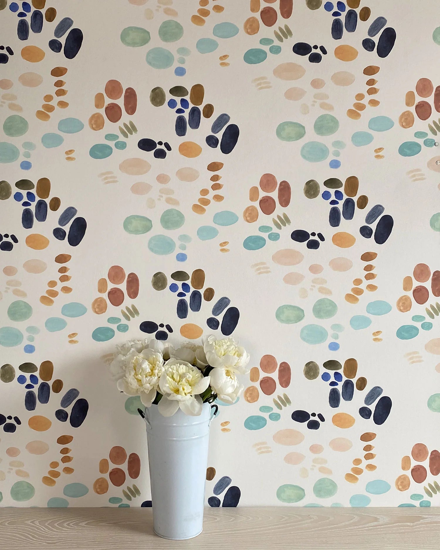 A vase of flowers stands in front of a wall papered in an abstract painterly print in turquoise, blue, orange and white.