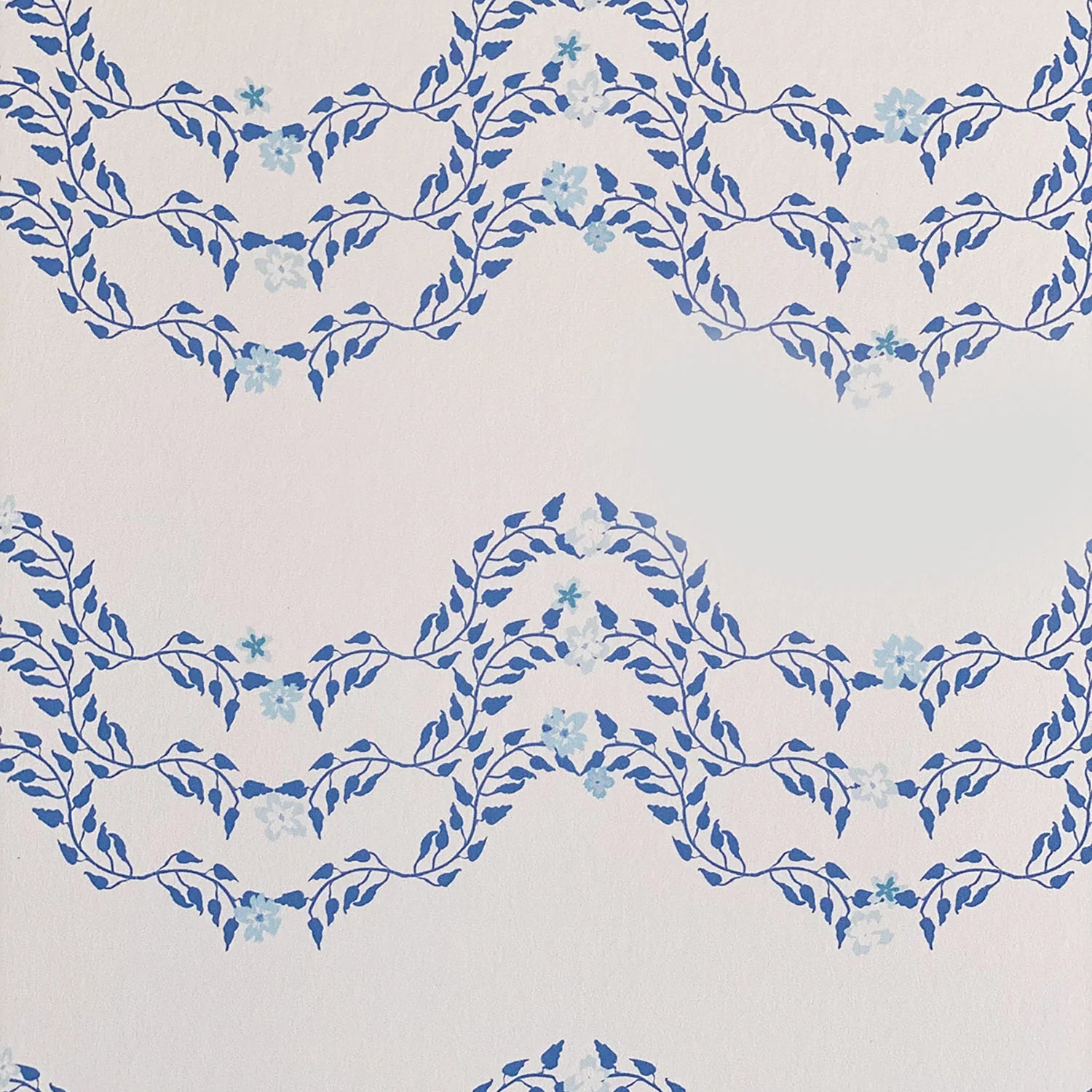 Detail of wallpaper in a curving floral stripe print in shades of blue on a cream field.