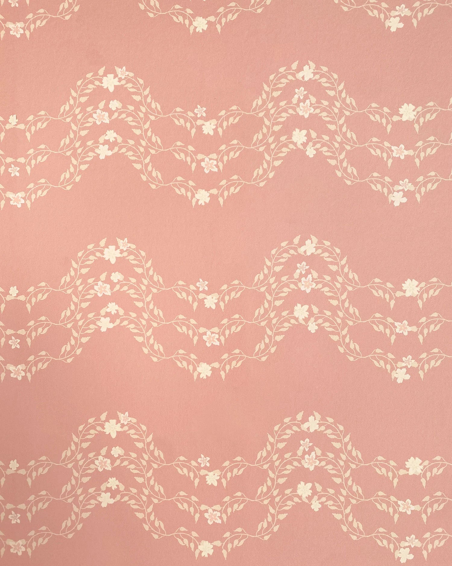 Detail of wallpaper in a curving floral stripe print in shades of cream on a pink field.