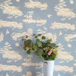 A vase of flowers stands in front of a wall covered in a playful illustrated car crash print in cream, white and light blue.