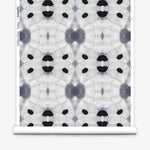 Partially unrolled wallpaper yardage in a watercolor ink blot print in shades of charcoal and black on a greige field.