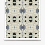 Partially unrolled wallpaper yardage in a watercolor ink blot print in shades of charcoal and black on a tan field.