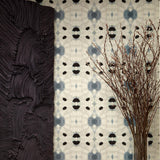 Flowers and a black room divider stand in front of a wall papered in a watercolor ink blot print in charcoal, black and tan.