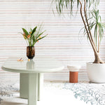 A modernist living space filled with plants and an accent wall papered in a painterly stripe print in pink, cream and white.