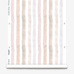 Partially unrolled wallpaper yardage in a painterly stripe print in shades of pink, gray and cream on a white field.