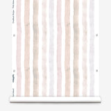 Partially unrolled wallpaper yardage in a painterly stripe print in shades of pink, gray and cream on a white field.