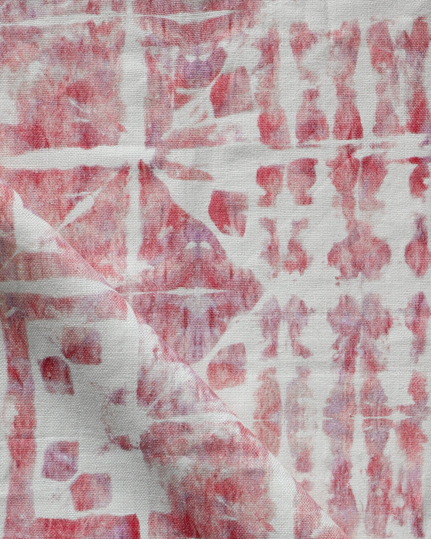 Detail of draped fabric in a watercolor dyed grid print in mottled white, pink and red.