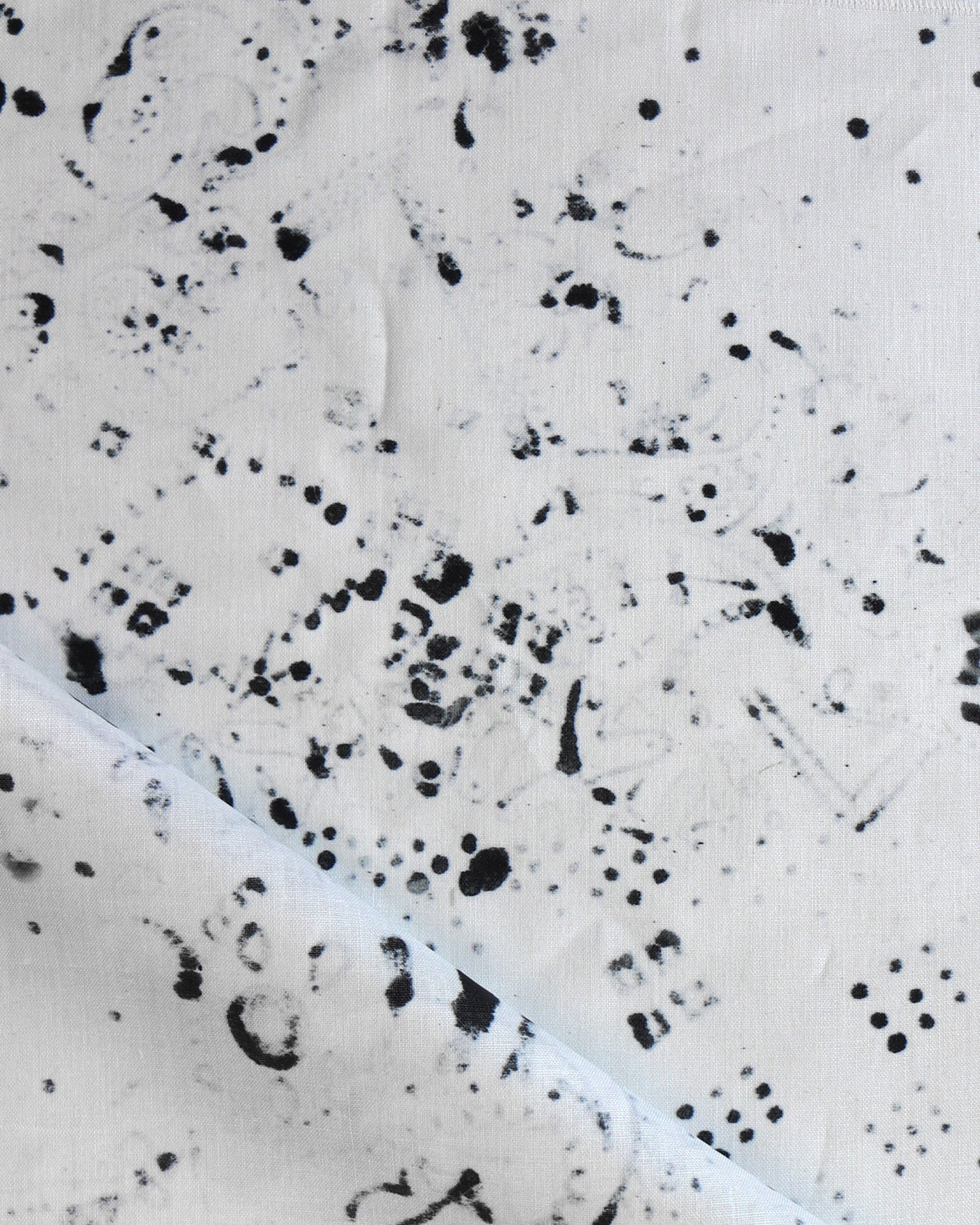 Detail of draped fabric in a painterly bandana print in black on a cream field.