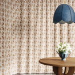 Floor length curtain in watercolor brown pattern with a wooden table with flowers and blue pendant lamp. 