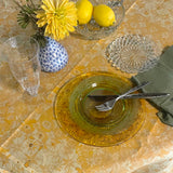 Dining table setting with yellow flowers, lemons, and glassware on a patterned tablecloth.