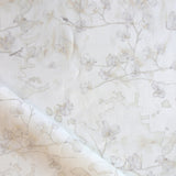 Draped fabric in a watercolor branch and floral pattern in beige on a white field.