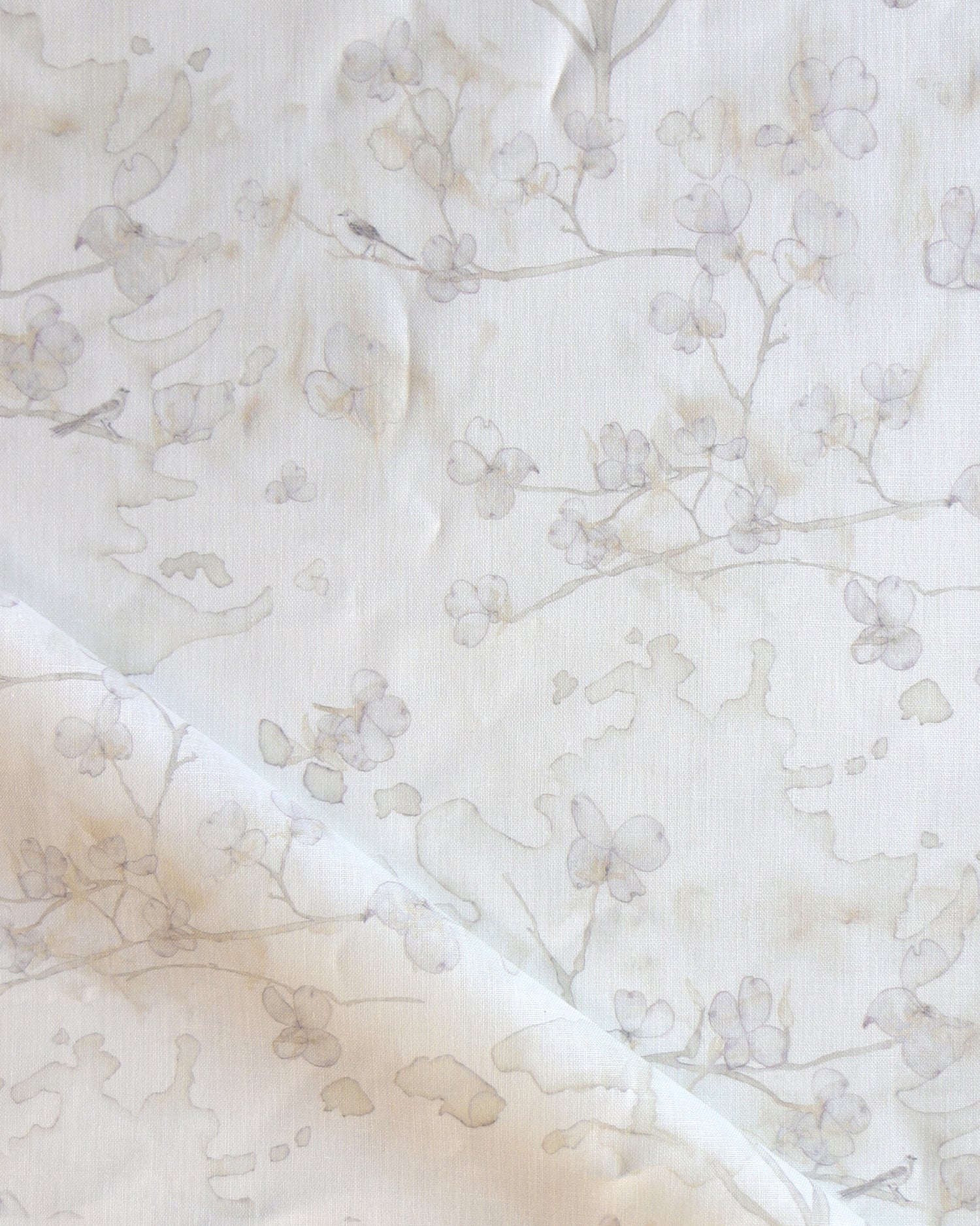 Draped fabric in a watercolor branch and floral pattern in beige on a white field.