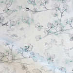 Draped fabric in a watercolor branch and floral pattern in teal green on a white field.