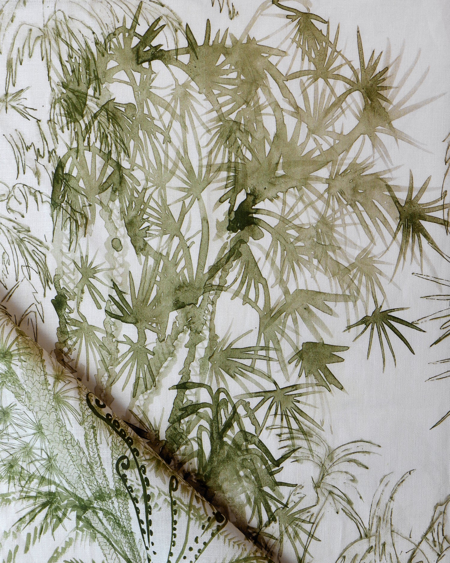 Detail of draped fabric in a painterly palm tree print in olive on a cream field.