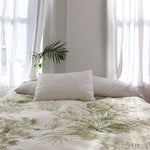 Bedroom interior with a bedsppread in a painterly palm tree print in olive on a cream field.