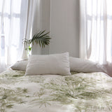 Bedroom interior with a bedsppread in a painterly palm tree print in olive on a cream field.