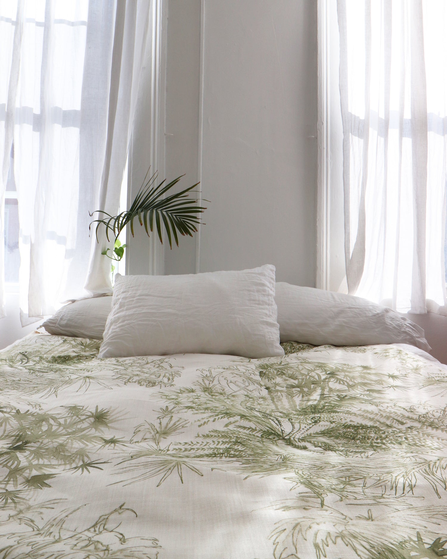 Bedroom interior with a bedsppread in a painterly palm tree print in olive on a cream field.