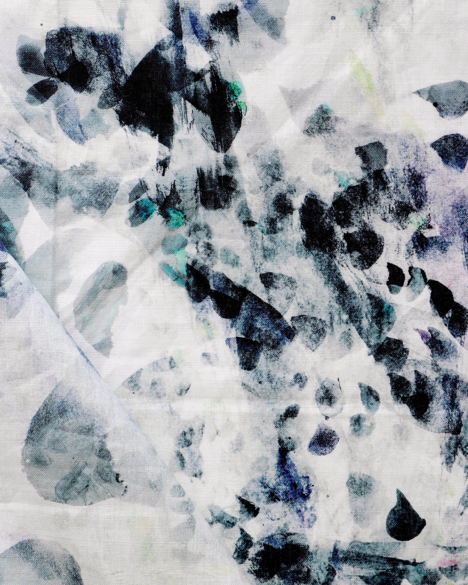 Detail of draped fabric in a watercolor paint blotch print in black, gray, blue and green on a white field.