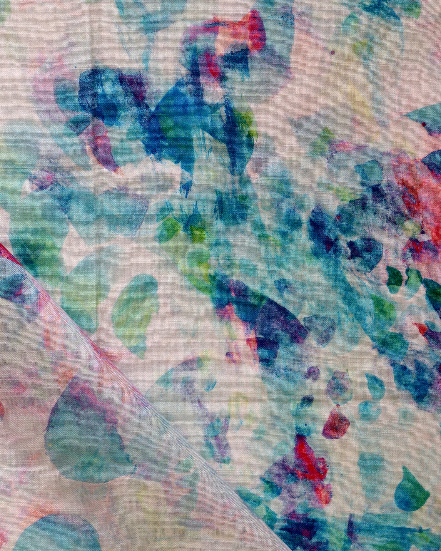 Detail of draped fabric in a watercolor paint blotch print in pink, green and turquoise on a white field.