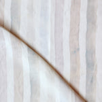 Detail of draped fabric in a painterly stripe print in shades of pink, gray and cream on a white field.