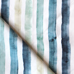 Detail of draped fabric in a painterly stripe print in shades of blue, green and tan on a white field.