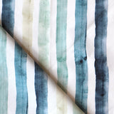 Detail of draped fabric in a painterly stripe print in shades of blue, green and tan on a white field.