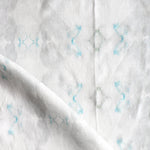 Detail of draped fabric in a striped ink blot print in shades of gray and turquoise on a cream field.