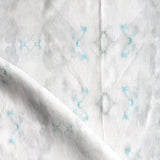 Detail of draped fabric in a striped ink blot print in shades of gray and turquoise on a cream field.