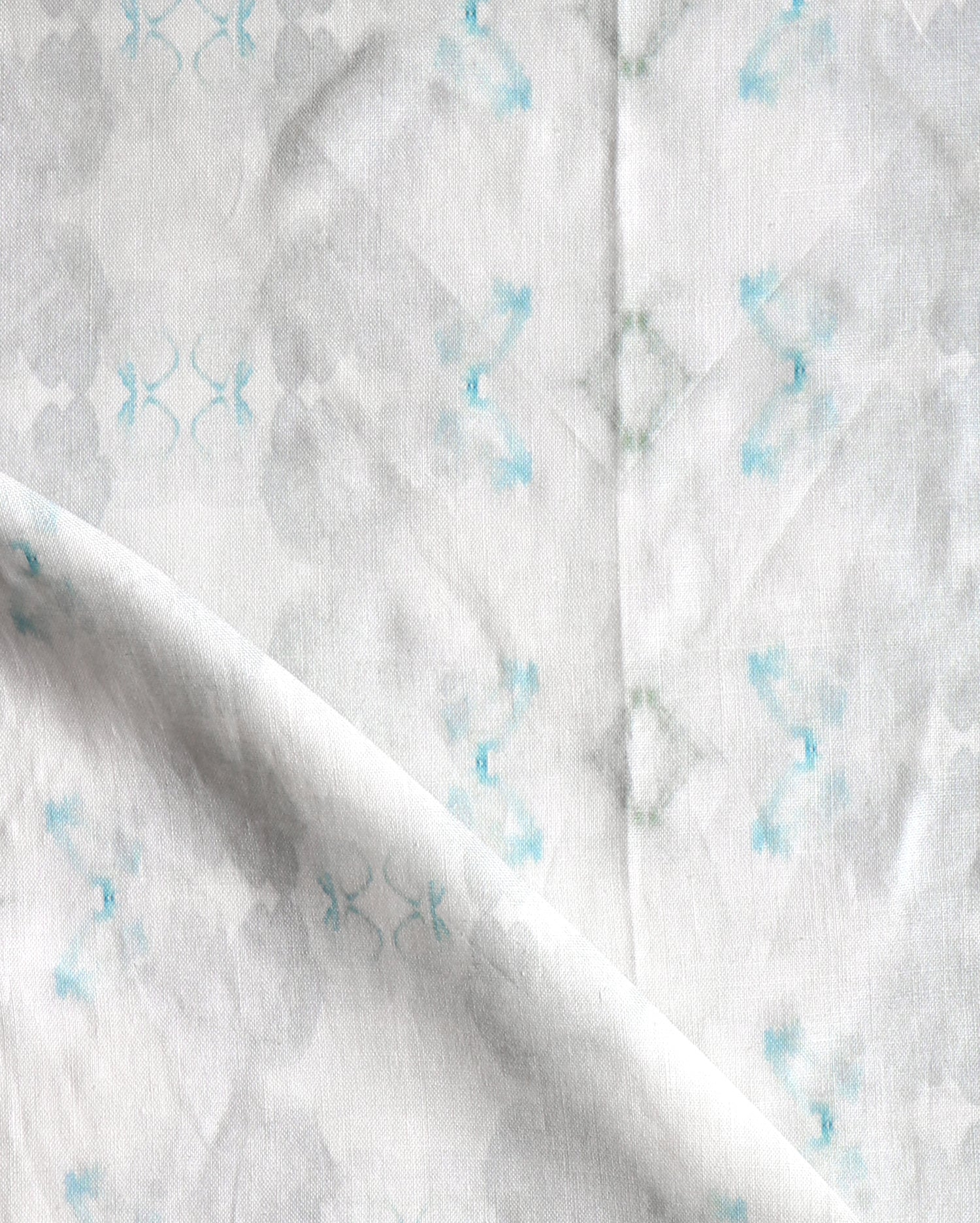 Detail of draped fabric in a striped ink blot print in shades of gray and turquoise on a cream field.
