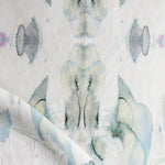 Detail of draped fabric in a watercolor paint blotch print in shades of gray and blue on a white field.