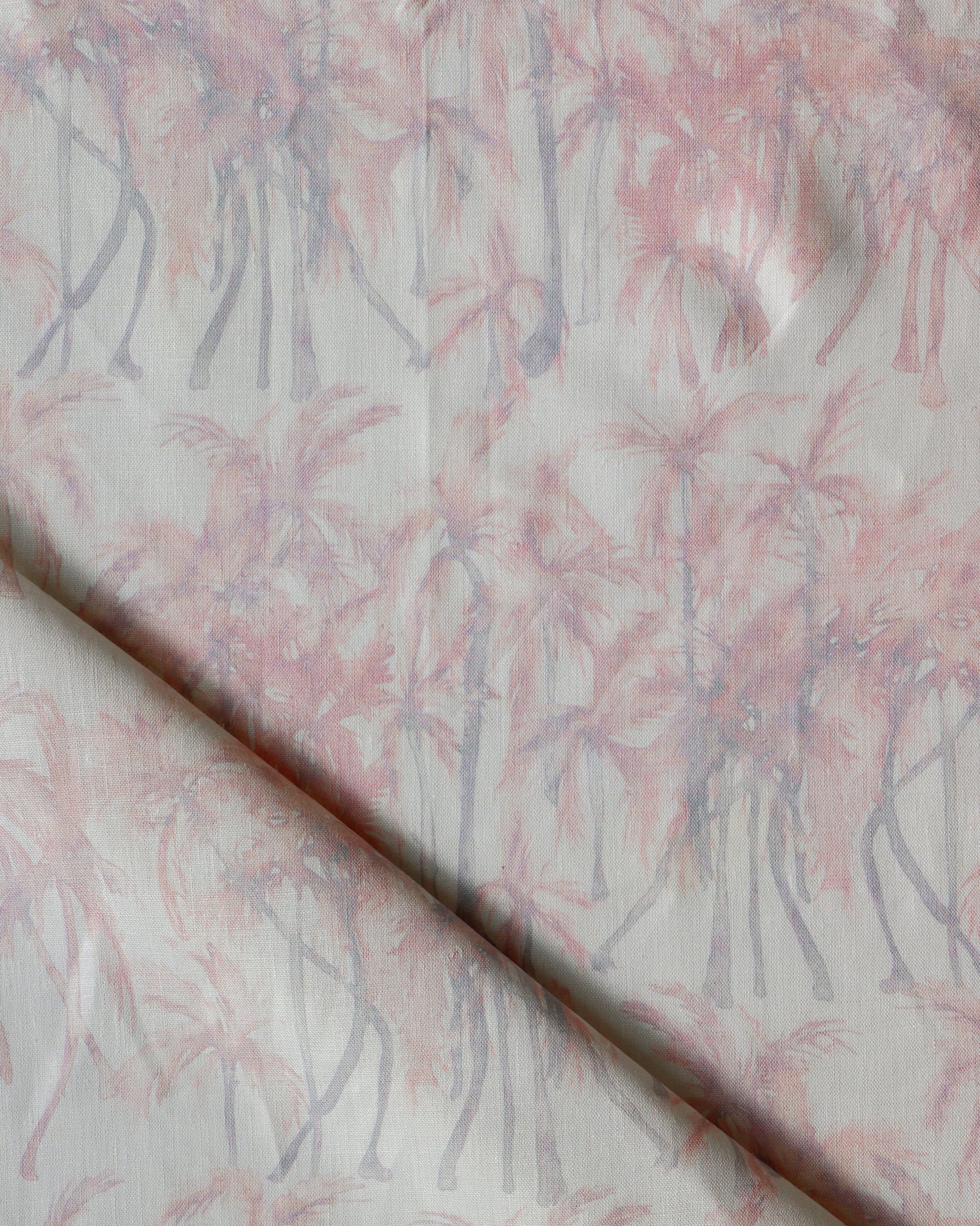 Detail of draped fabric in a painterly palm tree stripe print in shades of pink and gray on a white field.