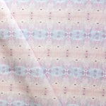 Detail of draped fabric in a gridded paint splatter print in shades of pink, blue, tan and white.