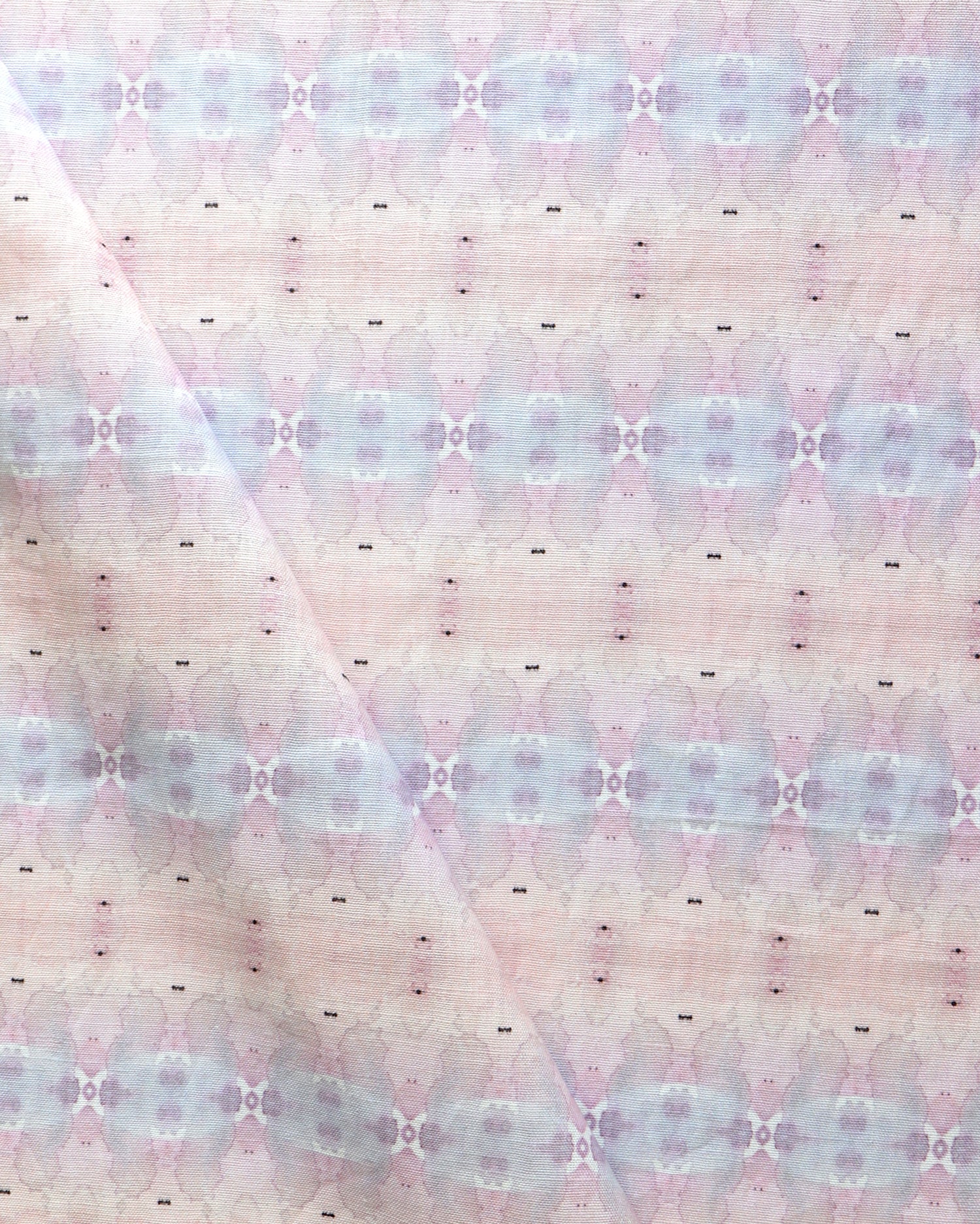 Detail of draped fabric in a gridded paint splatter print in shades of pink, blue, tan and white.