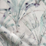 Detail of draped fabric in a painterly palm tree pattern in shades of green and purple on a tan field.
